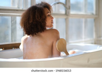 curly black girl laying, relaxing in the bath indoors. young woman relaxing in warm bathtub with foam and bubbles. Tired female enjoying rest pamper herself.