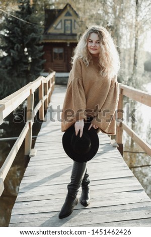curly blonde stands on the bridge; beautiful girl in black hat; blonde on sunset background

 