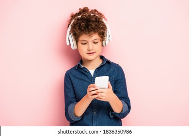 curly boy listening music in wireless headphones and using smartphone on pink - Powered by Shutterstock