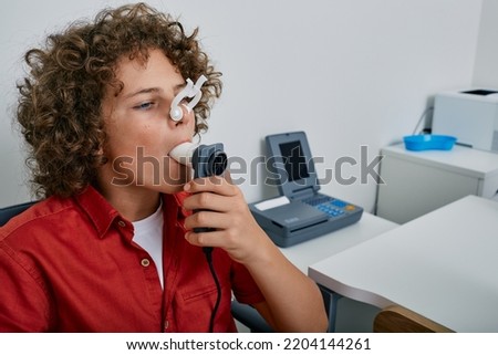 Curly boy performing pulmonary function test and spirometry using spirometer at medical clinic. Spirometry of child's lungs