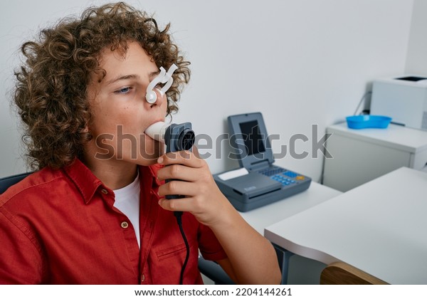 Curly boy performing pulmonary function test and\
spirometry using spirometer at medical clinic. Spirometry of\
child\'s lungs