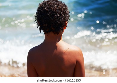 Curly Boy Staying By Back And Looking At The Sea. Boy On The Ocean.