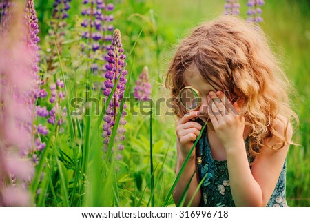 curly child girl exploring nature with loupe on summer walk