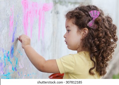 Curly Cute Baby Girl Drawing With Chalk On The Wall