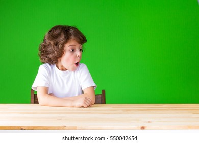 Curly Cute Boy With His Mouth Open Looking To The Left. Close-up. Green Background.