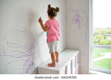 Curly Cute Little Baby Girl Drawing With Crayon Color On The Wall. Works Of Child