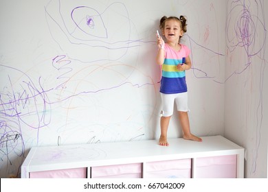 Curly cute little baby girl drawing with crayon color on the wall. Works of child