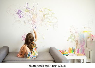 Curly cute little toddler girl painting with paints color and brush on the wall. Works of child