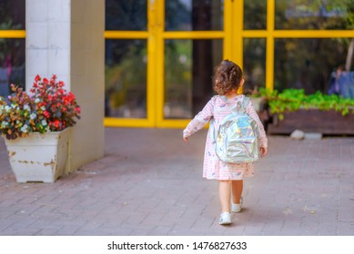 Curly cute little toddler girl back to school with holographic schoolbag or satchel, child going to kindergarten. Toddler kid first day at school or preschool. - Shutterstock ID 1476827633