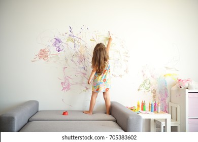 Curly cute little toddler girl painting with paints color and brush on the wall. Works of child