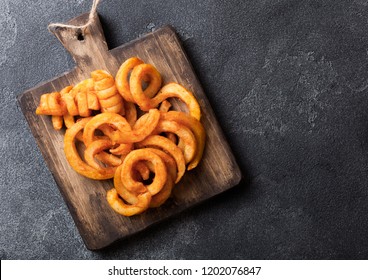 Curly fries fast food snack on wooden board on kitchen background. Unhealthy junk food