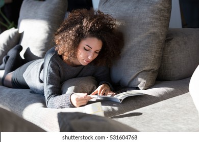 Curly Girl Reading Some Magazine Or Catalogue On A Big Sofa In Her Living Room