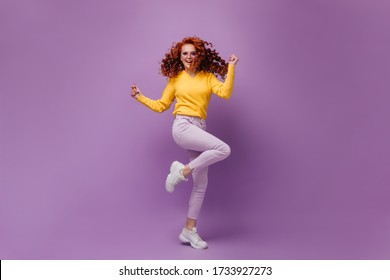 Curly Girl In Warm Sweater And Pants Jumping And Having Fun On Purple Background