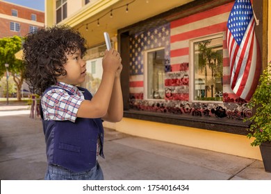 Curly hair boy takes a photo of an American flag on the building. The building has a framed painting of the American flag with outlined flower overlay with windows in the middle. - Powered by Shutterstock