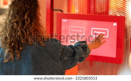 Curly hair woman using touch screen at the science exhibition. Taking interactive quiz in modern art museum.