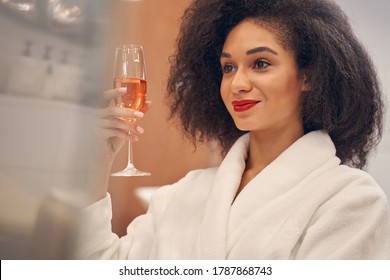 Curly haired fashionable woman glancing away while relaxing with a glass of champagne wine - Powered by Shutterstock