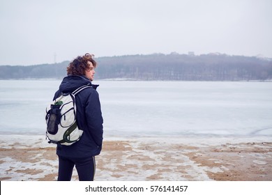 The curly haired man in a jacket with backpack winter at lake travels