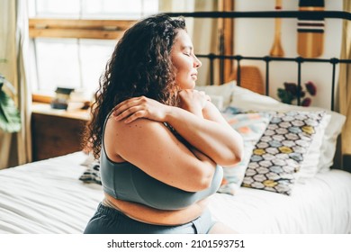 Curly Haired Overweight Young Woman In Grey Top And Shorts With Satisfaction On Face Accepts Curvy Body Shape Standing In Stylish Bedroom Closeup