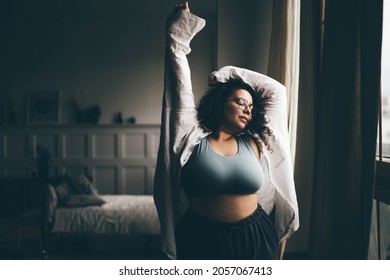 Curly haired plus size woman wearing comfortable clothes dances in stylish room. 