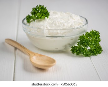 Curly leaves of parsley and a bowl of curd cream on a white table. The concept of a healthy diet. Curd cream