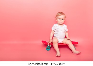 curly little baby girl child with red skateboard over pink background. concept sport.
