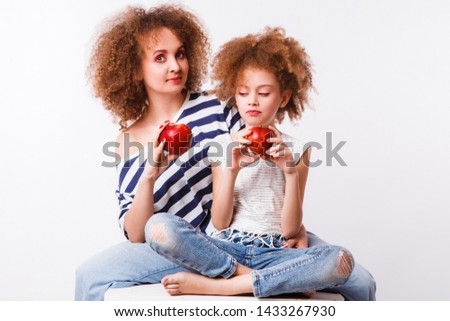 Curly mom and daughter eat big red apples on a light background.