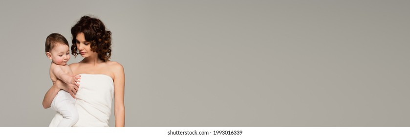 curly mother wrapped in towel holding son in arms isolated on grey, banner - Powered by Shutterstock