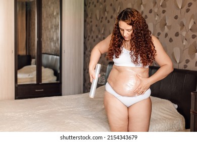 Curly Plus Size Woman In White Underwear Stand Near Bed In Bedroom And Wrap Sagging Belly With Cling Film. Fat Burning Treatment Of Thick Stomach. Weight Loss Program, Body Wrap Procedure.