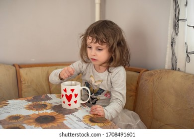 Curly Shaggy Brown-eyed Girl After Sleeping In The Morning. She Uses A Spoon To Stir The Sugar In The Tea, Which Is Poured Into A Cup With Red Hearts.