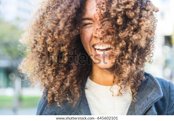 Curly woman laughing and shaking head. Smiling\
mixed race woman with curls having fun. Smart casual dress.\
Lifestyle and hairstyle\
concepts