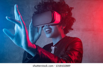 Curly Woman In Leather Jacket Using VR Glasses While Touching Air In Colorful Neon Lights 