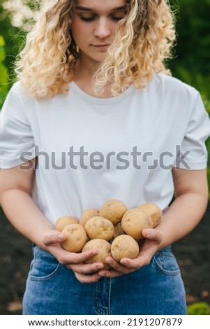 Curly woman in a white T-shirt holding young homemade potatoes in her hands. ealthy organic food, vegetables, agriculture, close up.