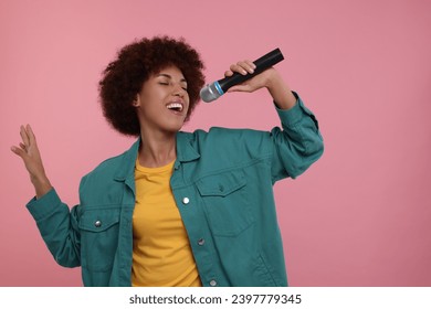 Curly young woman with microphone singing on pink background, space for text - Powered by Shutterstock