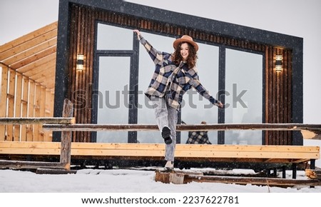 Curly young woman resting on terrace of modern barn house in the mountains. Happy female tourist enjoying winter holidays in new cottage. 商業照片 © 