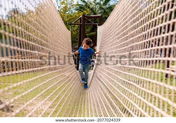 curly-haired boy crossing a net bridge.\
Development of the agility and courage of the\
child.