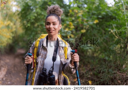A curly-haired forest wanderer, enjoying the serene atmosphere of an autumn forest trail, accompanied by her trusty binoculars.