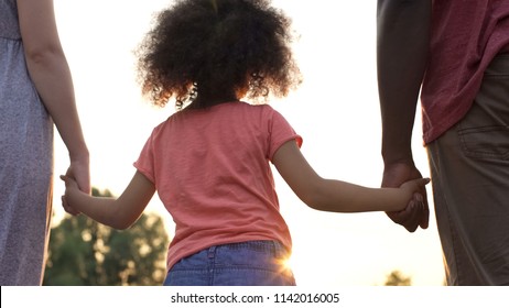Curly-haired girly holding her mother and father hands, happiness in family