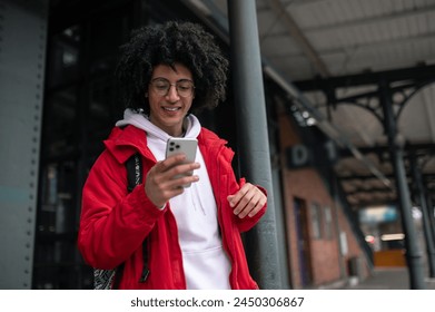 Curly-haired guy in eyeglasses with a phone in hands at the railway platform - Powered by Shutterstock