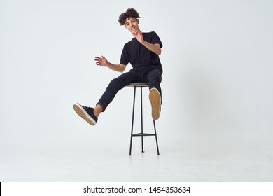 curly-haired man in a black t-shirt sits on a chair                               
