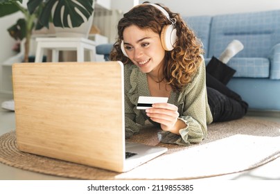 curly-haired woman with headphones, lying on the floor with laptop and credit card shopping online - Powered by Shutterstock