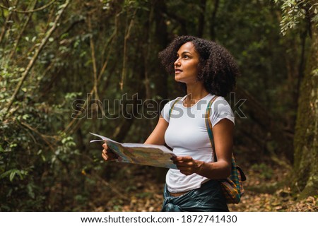 Curly-haired woman holding a map, tourist in the forest - Young brunette with white shirt holding and looking at the paper map, background of the jungle.