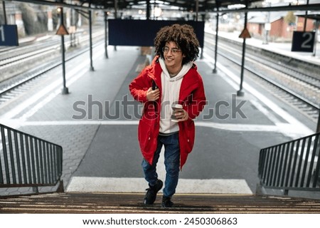 Curly-haired young guy in red jacket at the railway station