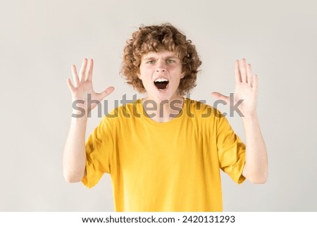 Curly-haired young man in distress and frustration is shown with his hands raised, screaming in desperation, expressing intense emotions and feeling overwhelmed.