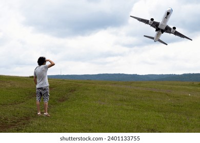 Curly-haired young man watches a plane taking off. Aviation. Domestic or international air transportation idea concept. Horizontal photo. People, human, person. 
