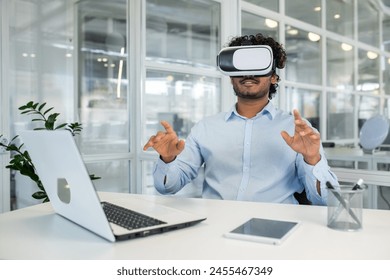 Curly-haired young professional immersed in virtual reality using a VR headset while engaging with invisible interfaces at his workplace equipped with various modern devices. - Powered by Shutterstock