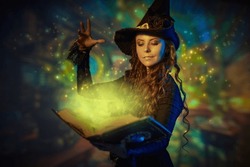 A Curly-haired Young Witch In A Black Hat And Black Dress Conjures With A Magic Book Of Spells. Wonderful World Of Magic. Halloween. Magical Background.
