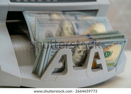 A currency counting machine accurately processes stacks of hundred-dollar bills in a busy financial institution, showcasing the efficiency of money handling.