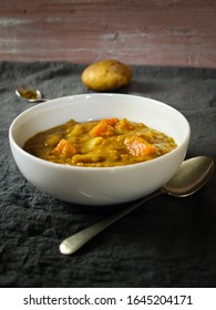 Curried Butternut Squash Soup On Dark Grey Linen With A Silver Spoon And Ingredients In The Background.