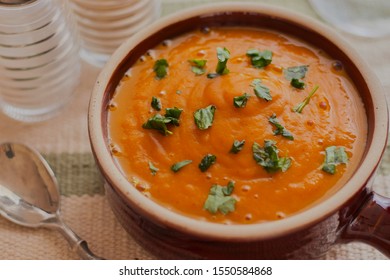 Curried Butternut Squash Soup,served In A Brown Pot With Coriander Sprinkled On Top.