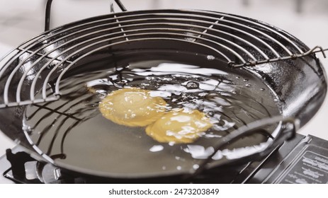 Curry puff cake is in the process of being fried in a black frying pan and portable stove.
